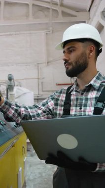 Yetenekli endüstriyel mühendis imalat sürecini denetliyor, otomatik makineleri dizüstü bilgisayarla kontrol ediyor, modern fabrika ortamında üretim verimliliğini ve kalitesini sağlıyor.