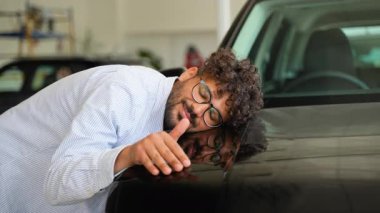 Gururlu araba sahibi yeni satın alınan arabayı nazikçe okşuyor, mutluluk ve memnuniyet saçarak lüks galeri galerisinde duruyor, kişisel başarıları ve otomotiv hayallerini simgeliyor.