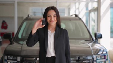 Araba anahtarlarını elinde tutan ve yeni alımını bir araba galerisinde kutlayan coşkulu iş kadını, amacına ulaşma sevincini ve heyecanını dile getiriyor.
