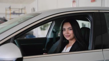 Başarılı bir iş kadını modern aracın içinde otururken araba anahtarını sunuyor, lüks galeride otomotiv alımını kutluyor.