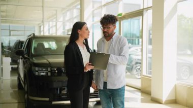 Profesyonel satış elemanı, araç özelliklerini ve satın alma anlaşmasının detaylarını erkek müşteriye sunar, araba satın alma sürecinde güven ve şeffaflığı teşvik eder