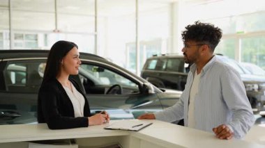 Profesyonel araba satıcısı, memnun müşterilerle başarılı satış işlemlerini sonuçlandırıyor, şirket tokalaşması ve araç anahtarlarını modern galeri galerisi içinde transfer ediyor.