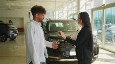 Yeni aracın başarılı bir şekilde satın alınması, satış elemanının müşteriye anahtarları vermesi, el sıkışması ve modern araba galerisinde anlaşmanın sonuçlanması.