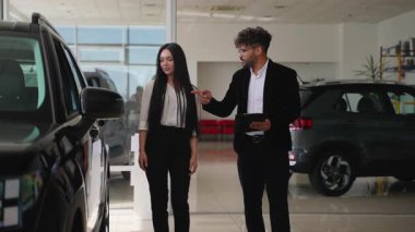 Modern bir bayilikte yeni bir siyah jipin özelliklerini gösteren ve açıklayan profesyonel bir satıcı, finansman seçenekleri ve satın alma anlaşmalarını tartışıyor.