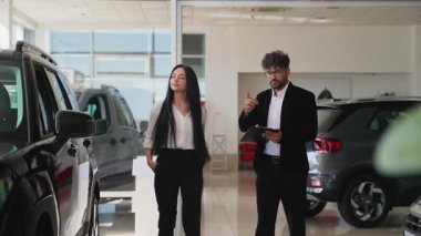 Modern bir otomobil galerisinden yeni bir araç seçmede müşteriye yardımcı olan profesyonel satıcı, özellikler ve finansman seçenekleri hakkında danışmanlık ve bilgi sunar