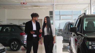 Profesyonel araba satıcısı, galeri içindeki potansiyel alıcılara yeni araç özelliklerini gösteriyor, finansman seçeneklerini gözden geçiriyor ve otomobil detaylarını tartışıyor.