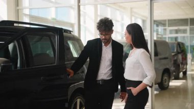 Modern bayilikte potansiyel alıcıya yeni araç özellikleri gösteren profesyonel bir araba satıcısı, araba sahibi olmanın faydalarını ve avantajlarını anlatıyor.