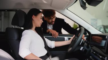 Modern bir araba galerisinde profesyonel bir araba satıcısı potansiyel bir kadın müşteriye yeni bir arabanın özelliklerini anlatıyor.