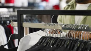 Moda perakende işçisi modern giyim mağazasında beyaz t-shirt 'ü kontrol ediyor, kalite ve tasarımı inceliyor ve rafa geri koyuyor.