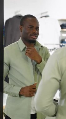 Afro-Amerikan erkek, şık bir perakende satış ortamında yeni kıyafet alımından tatmin olurken, görünüşü kontrol ederken gömlek yakasını düzeltiyor.