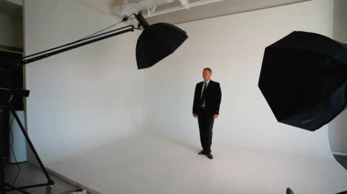Sahne arkasında profesyonel bir fotoğrafçıya bakın. Yakışıklı, olgun bir iş adamının portrelerini çekiyor. Modern, iyi donanımlı bir stüdyoda duruyor.