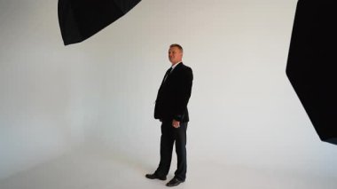 Profesyonel bir stüdyo fotoğraf çekiminde siyah takım elbiseli, kendinden emin bir erkek girişimci kameraya poz veriyor.