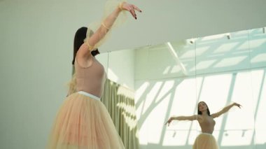 Güzel bir elbiseyle zarif bir balerin. Parlak, güneşli bir stüdyoda dans provası yapıyor. Büyük aynaları var.