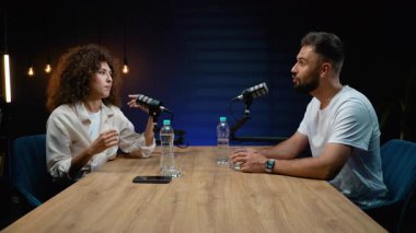 Erkek ve kadın radyo sunucuları profesyonel bir stüdyodan canlı yayında konuşmalarını dostça bir tokalaşma ve anlaşmaya vardıktan sonra gülümsemeyle bitiriyorlar.