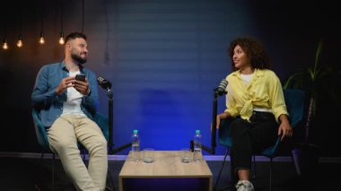 Çeşitli erkek sunucu ve kadın konuk bir ses podcast 'i kaydediyor ya da modern bir stüdyoda radyo talk show' u canlı yayınlıyor, mikrofonların önünde otururken ilgi çekici bir konuşma yapıyorlar.