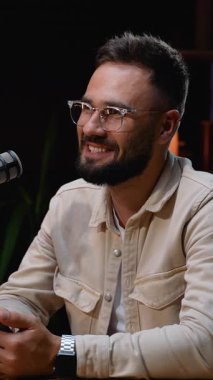 Gözlüklü, mikrofona konuşan ve podcast tartışmasına katılırken gülümseyen, stüdyodaki izleyicilerle hikayeler ve sezgiler paylaşan pozitif sakallı bir adam.