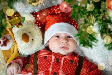 Yeni doğmuş bir bebeğin Noel ağacının altında oyuncak ayıyla yatışı, Noel ışıklarıyla Noel havası bokeh. Yukarıdan görüntüle