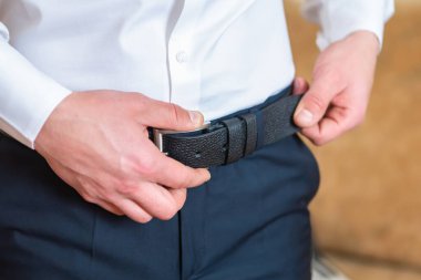 Resmi bir gömlek ve pantolon giymiş bir adam siyah kuşağını takıyor, özel bir durum için hazır..