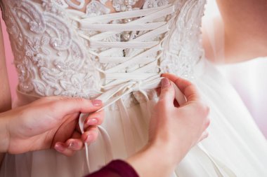 Geline, gelinliğinin karmaşık bağcıklarını düzeltmesi için bir arkadaşı yardım eder..