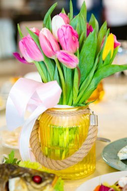 A beautiful arrangement of tulips in a jar adorned with a ribbon enhances the dining table filled with gourmet cuisine. clipart