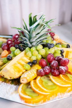 Ananas, üzüm, portakal ve kivi de dahil olmak üzere güzel bir şekilde düzenlenmiş taze meyve tabağı şenlikli bir ortamda canlı renkler sergiliyor..