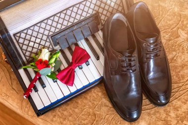 A stylish arrangement of a bow tie, boutonni re, and polished shoes placed on a piano, symbolizing wedding preparations. clipart