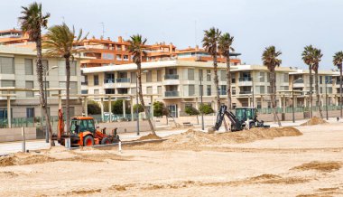 Heavy machinery is seen working on a sandy beach near residential buildings in a coastal setting. clipart