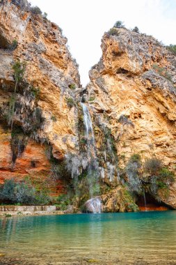 Uçurumun kenarından sersemletici bir şelale akar ve altında canlı turkuaz bir su bulunan görkemli bir manzara yaratır..