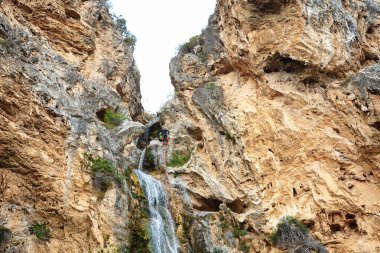 Maceracı bir dağcı engebeli arazide çağlayan bir şelalenin yanında dik bir kaya yüzeyine tırmanıyor..