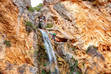 Çarpıcı bir şelale, canlı yeşilliklerle bezenmiş engebeli uçurumlardan aşağı akar ve huzurlu bir doğal ortam yaratır..