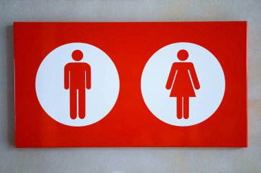 Kırmızı arka planda erkek ve kadın tuvalet sembollerini gösteren bir tabela, ziyaretçiler için açık bir yön sağlıyor.
