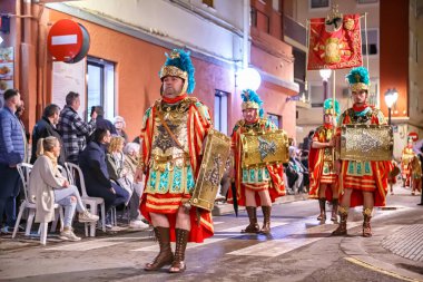 Akşamları, kalabalık bir caddede geleneksel kıyafet yürüyüşüne katılanlar etrafı izleyiciler ve atmosferik aydınlatmalarla çevrili..