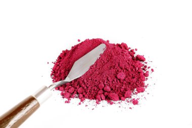 Bir kap devrildi, beyaz bir yüzeye parlak kırmızı toz saçıyor, maddenin canlı rengini ve dokusunu gösteriyor..