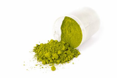 Parlak yeşil bir toz beyaz bir kaptan temiz beyaz bir yüzeye dökülüyor, canlı rengini ve dokusunu gösteriyor..