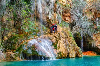 Dört maceraperestten oluşan bir grup kayalık bir çıkıntının üzerinde duruyor, aşağıdaki turkuaz bir lagünün içine dökülen güzel şelaleye hayret ediyorlar..