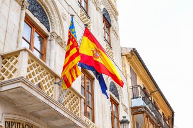 İspanya, Valencia, 29 Mart 2024: Valencia 'daki tarihi bir binadan renkli bayraklar dalgalanıyor, açık gökyüzü altında bölgesel gurur ve birlik gösteriliyor.