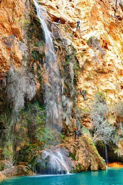 Heyecan arayanlardan oluşan bir grup, canlı kaya oluşumları ve yeşilliklerle çevrili dik bir şelaleye iniyor..