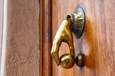 İspanya, Valencia, 29 Mart 2024: Bir el şeklinde dekoratif pirinç kapı tokmağı ahşap bir kapı üzerinde yuvarlak bir zile vurmaya hazırdır..