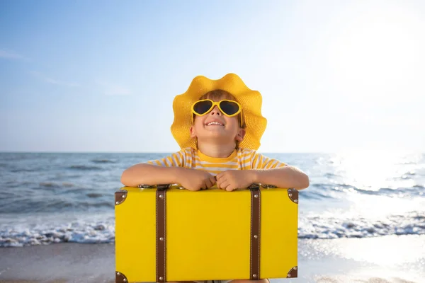 青空を背景に太陽を楽しむ幸せな子供 ビーチで楽しんでいるスーツケース付きの子供 夏休み 休日のコンセプト — ストック写真