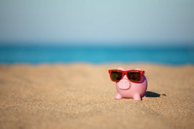 Piggybank on the beach against sea and sky background. Savings for summer travel and vacation concept clipart
