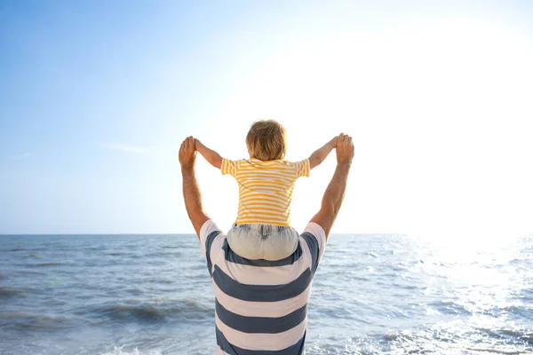 幸せな家族はビーチで楽しんでいます 青い海と空の背景に対する父と息子 夏休みと父親の日の概念 リアビューポートレート — ストック写真