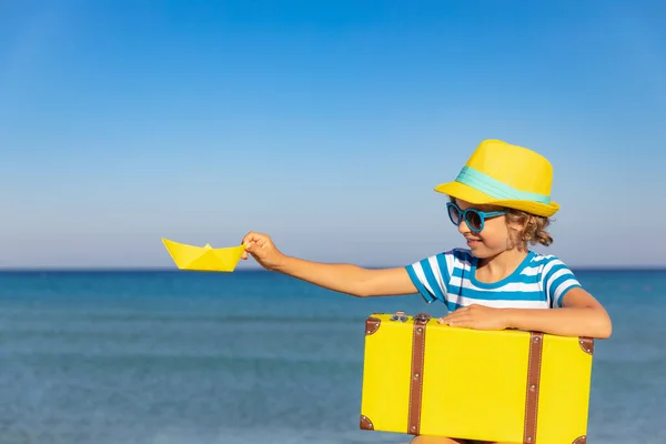 暑假带着老式手提箱的孩子 在海滩上玩得开心的女孩 有纸船的孩子坐在大海和天空的背景下 旅行和探险概念 — 图库照片