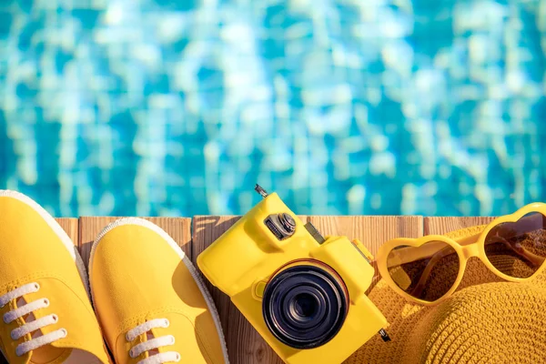 水の背景に対して青い木の上に黄色のスニーカーとカメラ 夏休みと旅行のコンセプト — ストック写真