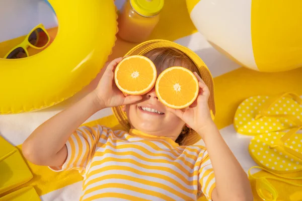幸せな子供のサングラスのようなオレンジの果物のスライスを保持 子供の縞模様のTシャツビーチタオルの上に横たわるを着て 健康的な食事と夏休みのコンセプト — ストック写真