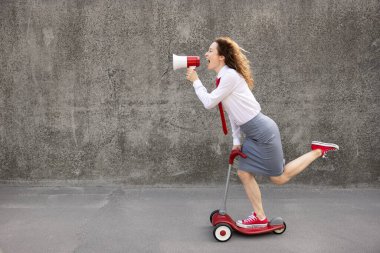 Scooter kullanan mutlu bir iş kadını. Hoparlörden bağıran genç bir kadının açık hava portresi. İşe dön, işe başla ve iş fikri kavramı