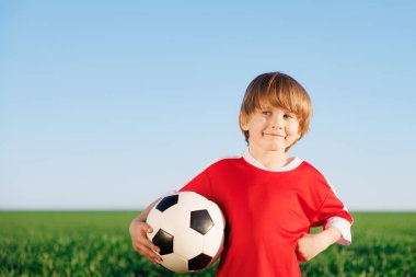 Mutlu çocuk futbolcu gibi davranıyor. Dışarıdaki çocuğun portresi. Çocuk yeşil alana karşı. Başarı ve kazanan konsepti