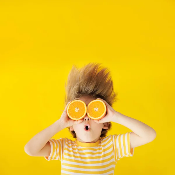 高傲的孩子手里拿着像太阳镜一样的橘子片 孩子穿着条纹黄色T恤 背对着蓝纸背景 健康饮食和暑假概念 — 图库照片