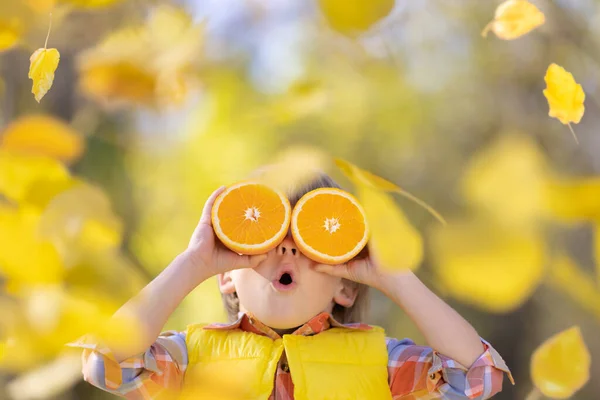 惊讶的孩子手里拿着像太阳镜一样的橘子片 秋天里有趣的孩子模糊了背景 秋天的户外快乐男孩 健康饮食概念 — 图库照片