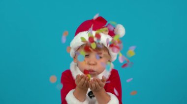 Happy child blowing confetti. Funny kid wearing Christmas costume against blue background. Xmas holiday concept. Slow motion