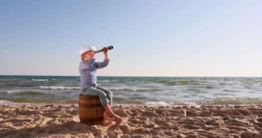 Happy child pretend to be sailor. Kid having fun at beach. Boy looking through spyglass. Summer vacation and travel concept. Slow motion